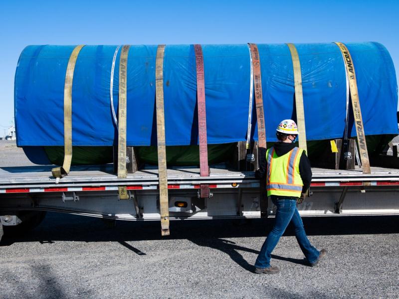 A nuclear fuel canister, wrapped in a blue tarp, sits atop a flatbed truck just outside the PNNL Richland campus.