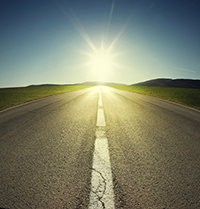 a road with midline marker leading to a sunset