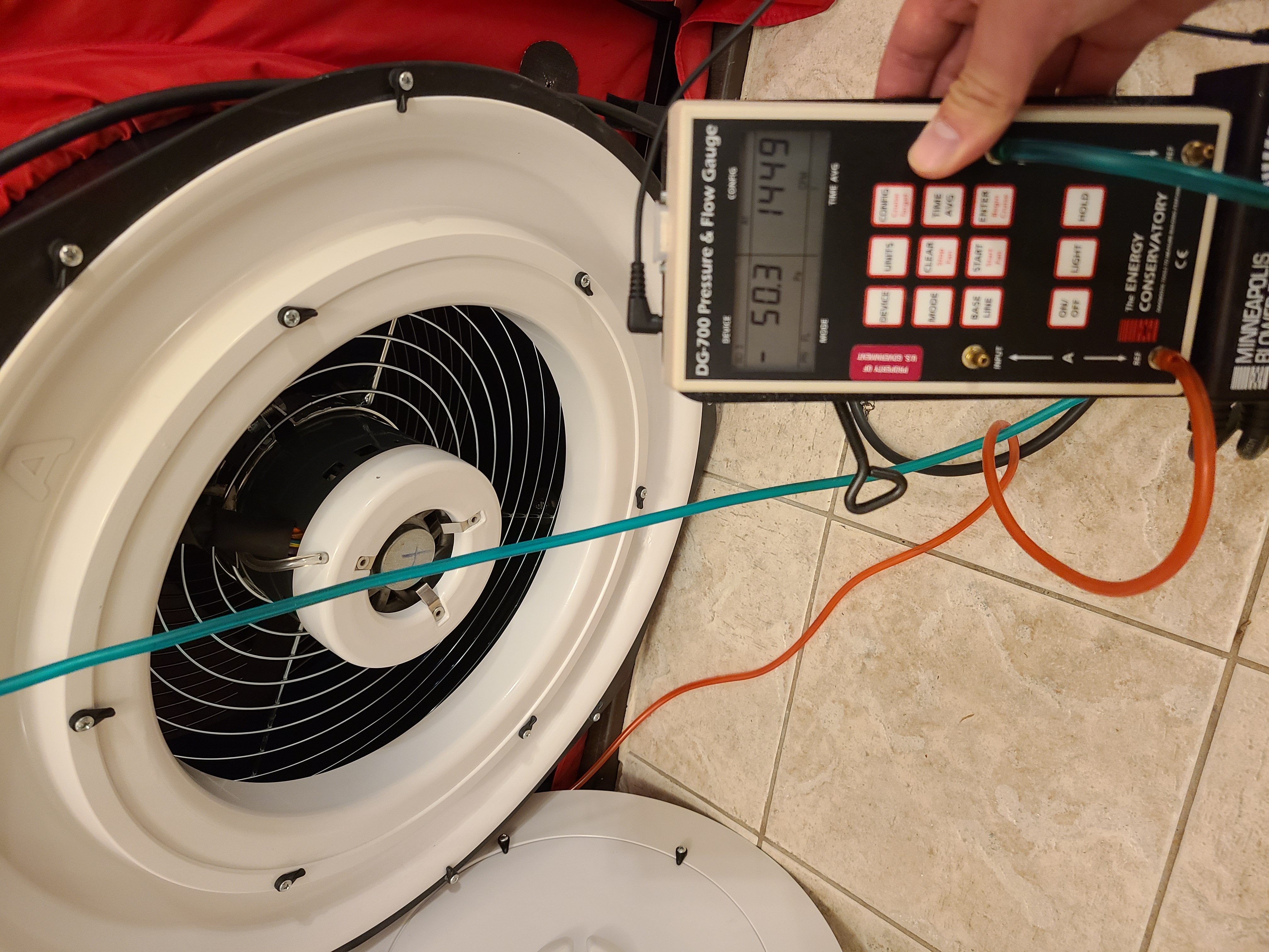 A pressure and flow gauge device with a digital display and keypad, connected by wires to a device with a fan