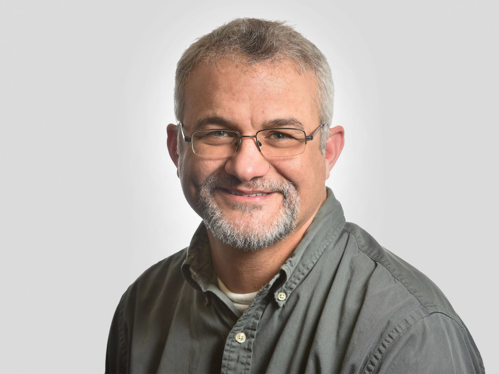 Smiling white man in gray shirt with gray hair/beard and glasses