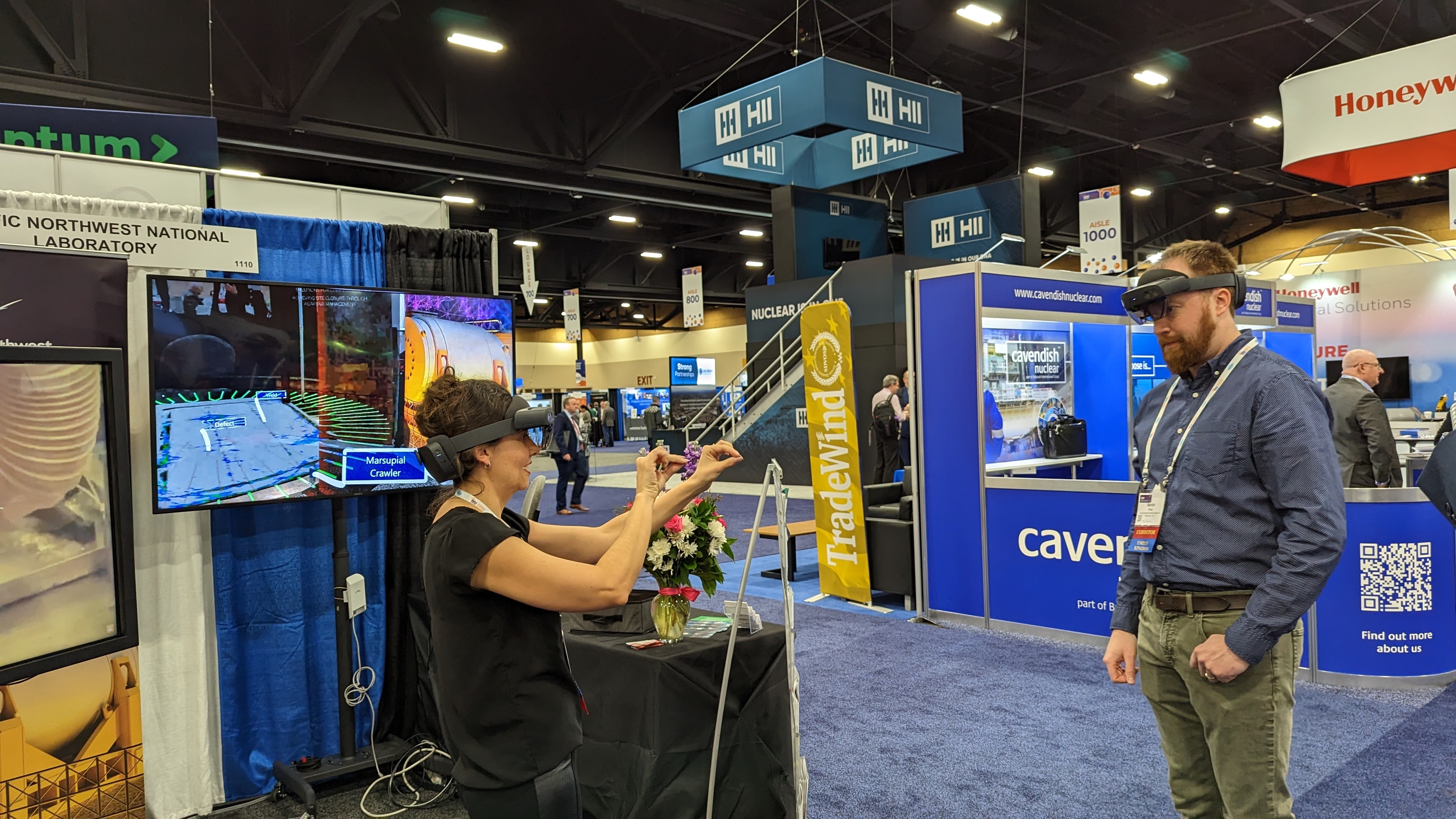 Two people use augemented reality headsets at PNNLs booth at WM2023