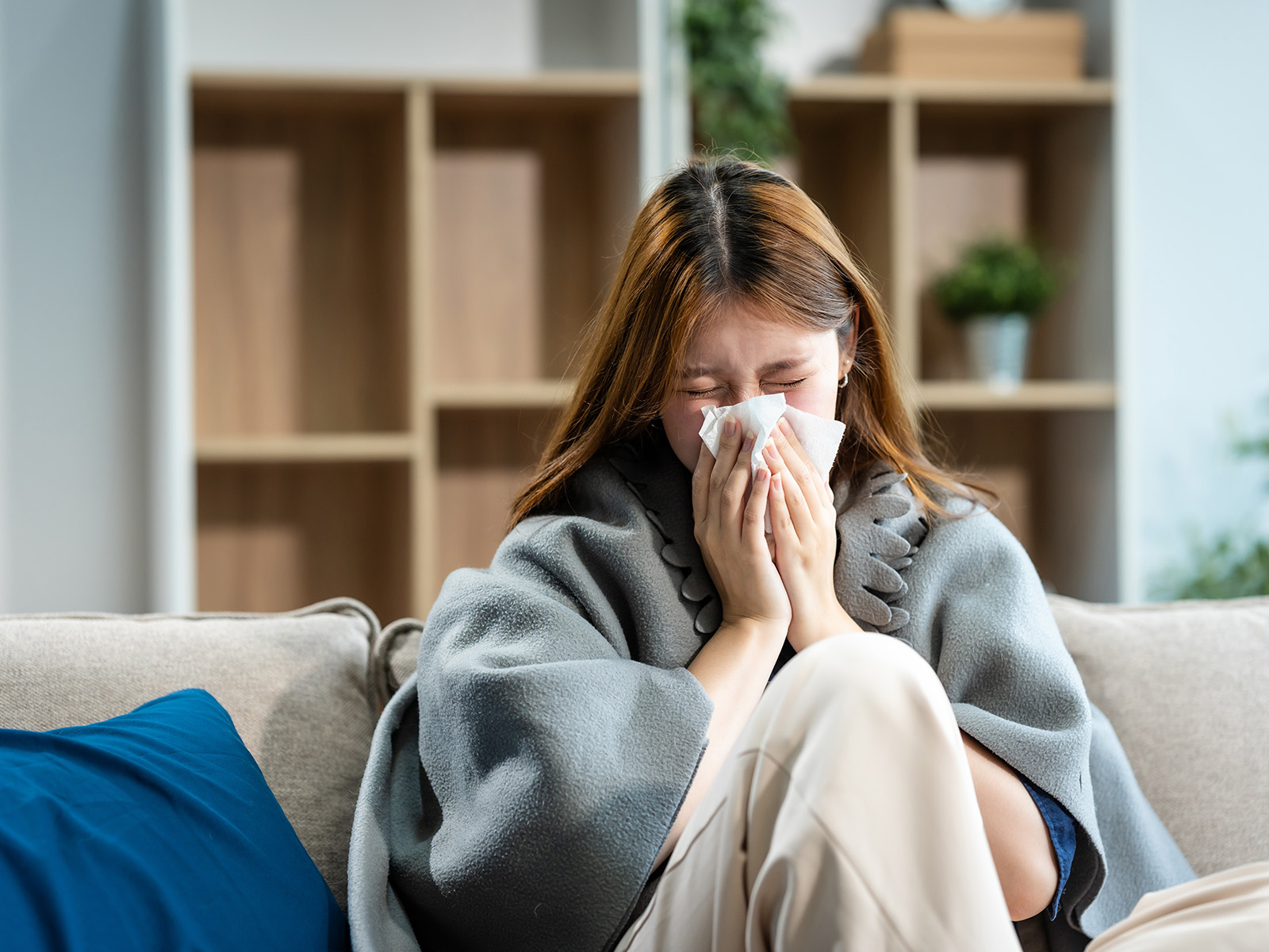 A woman covered with a blanket sneezes.