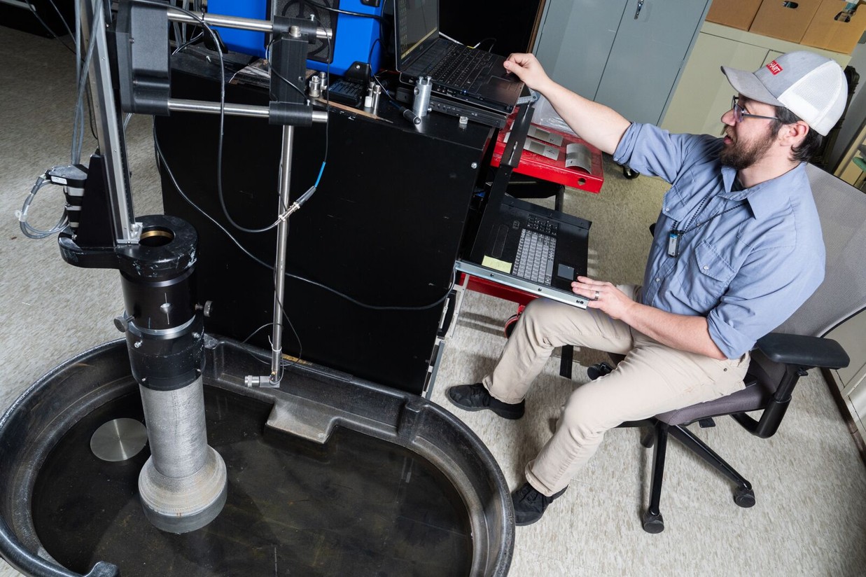 Man sitting in a chair looking at a computer screen next to 3D imaging equipment