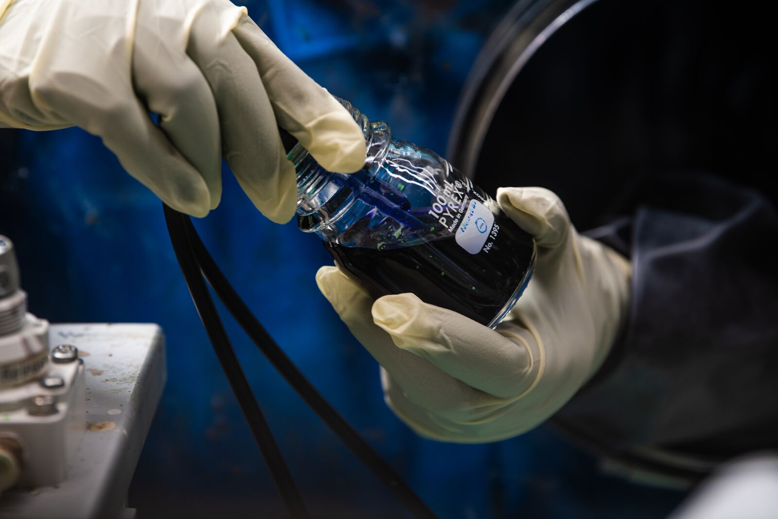 Close-up photo of a researcher sticking a wired prod into a small container of dark liquid