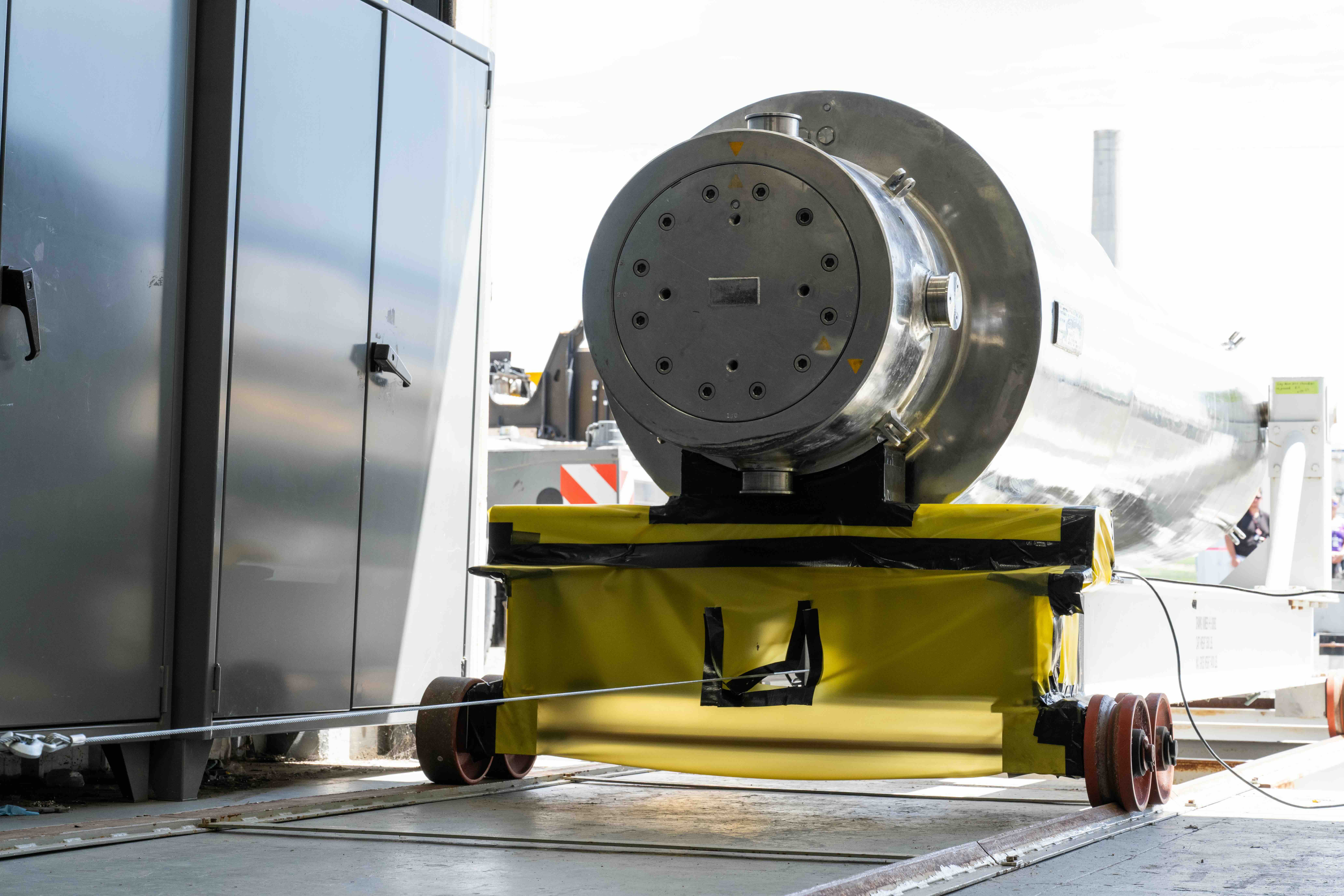 A 19-foot-long, chrome canister sits atop a long cart, which is pulled by a metal wire along a track into the radiochemical processing laboratory.