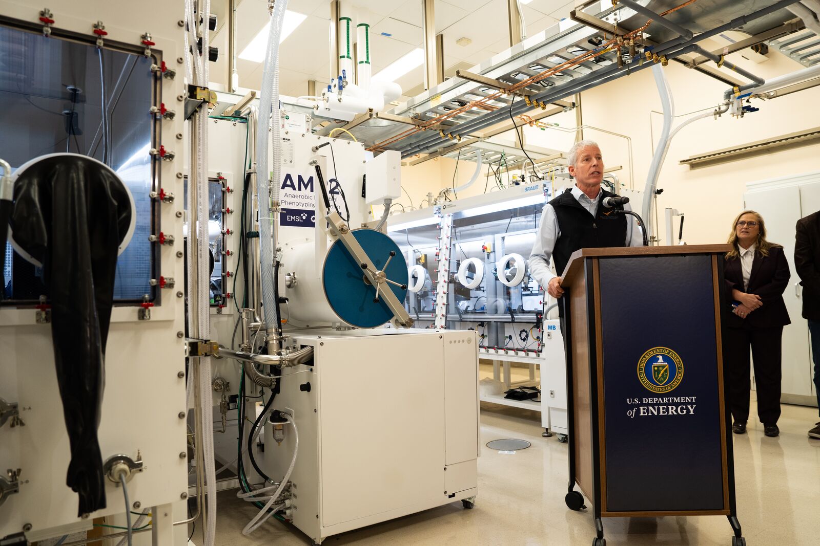 DOE Secretary Chris Wright speaking at a podium in front of the Anaerobic Microbial Phenotyping Platform.