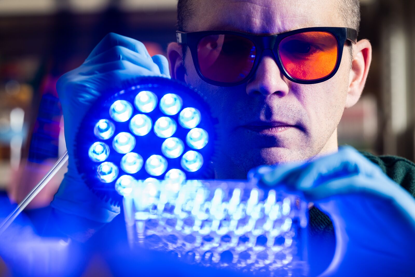 PNNL Researcher Joshua Elmore holding up a light to a tray while wearing safety gloves and glasses.
