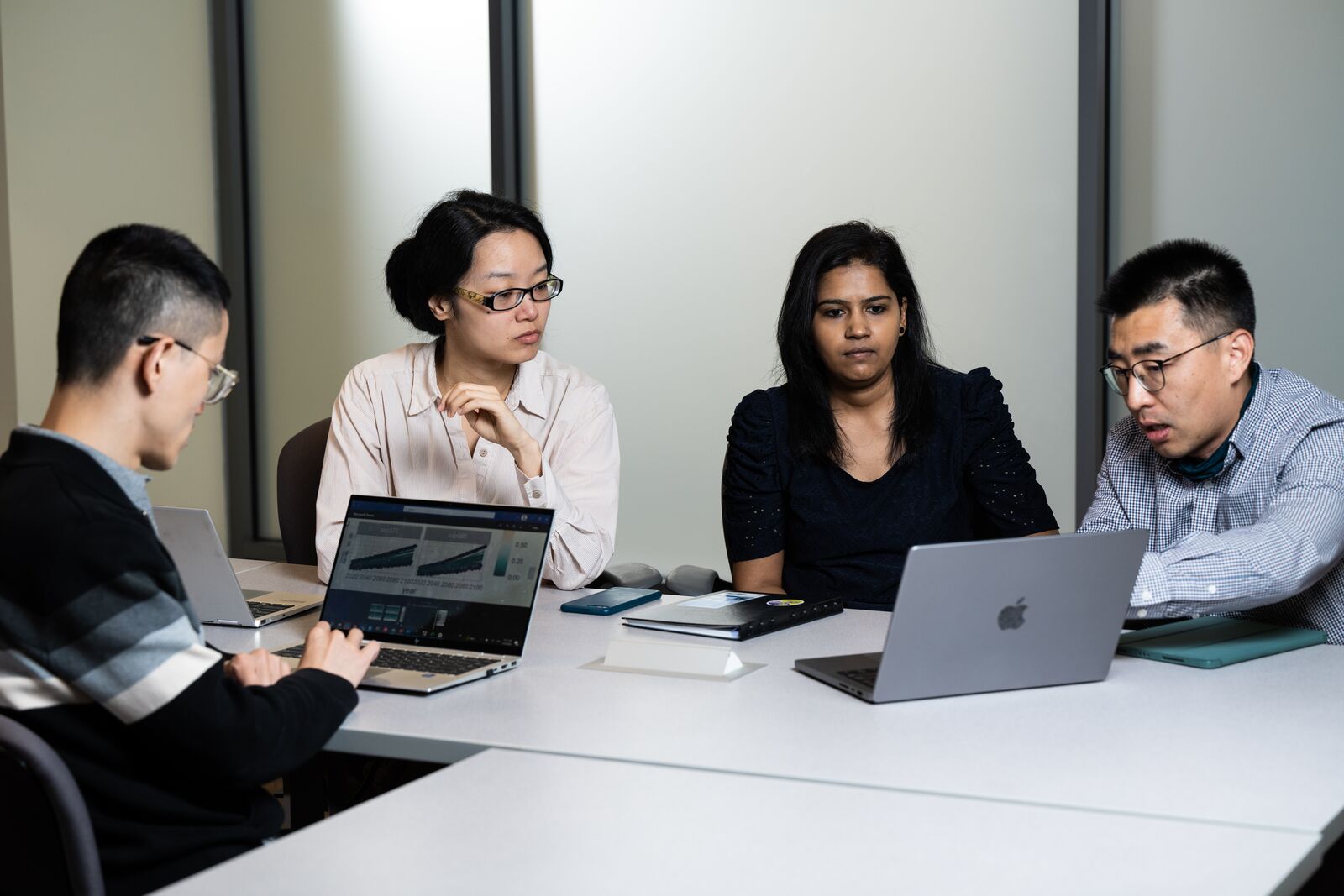 Photo of four people sitting at a table, talking and using computers.