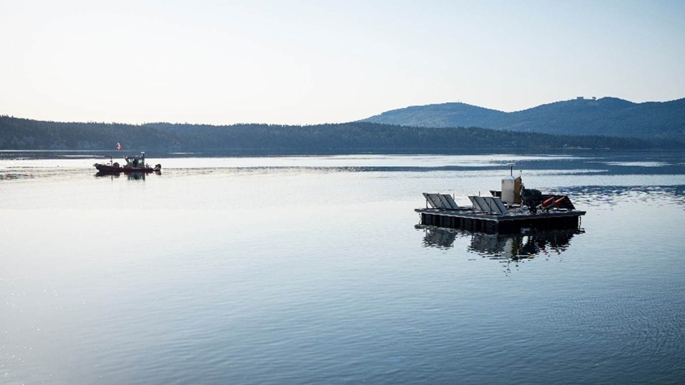 a floating platform on Sequim Bay with solar panels, in the distance a research vessel on the water