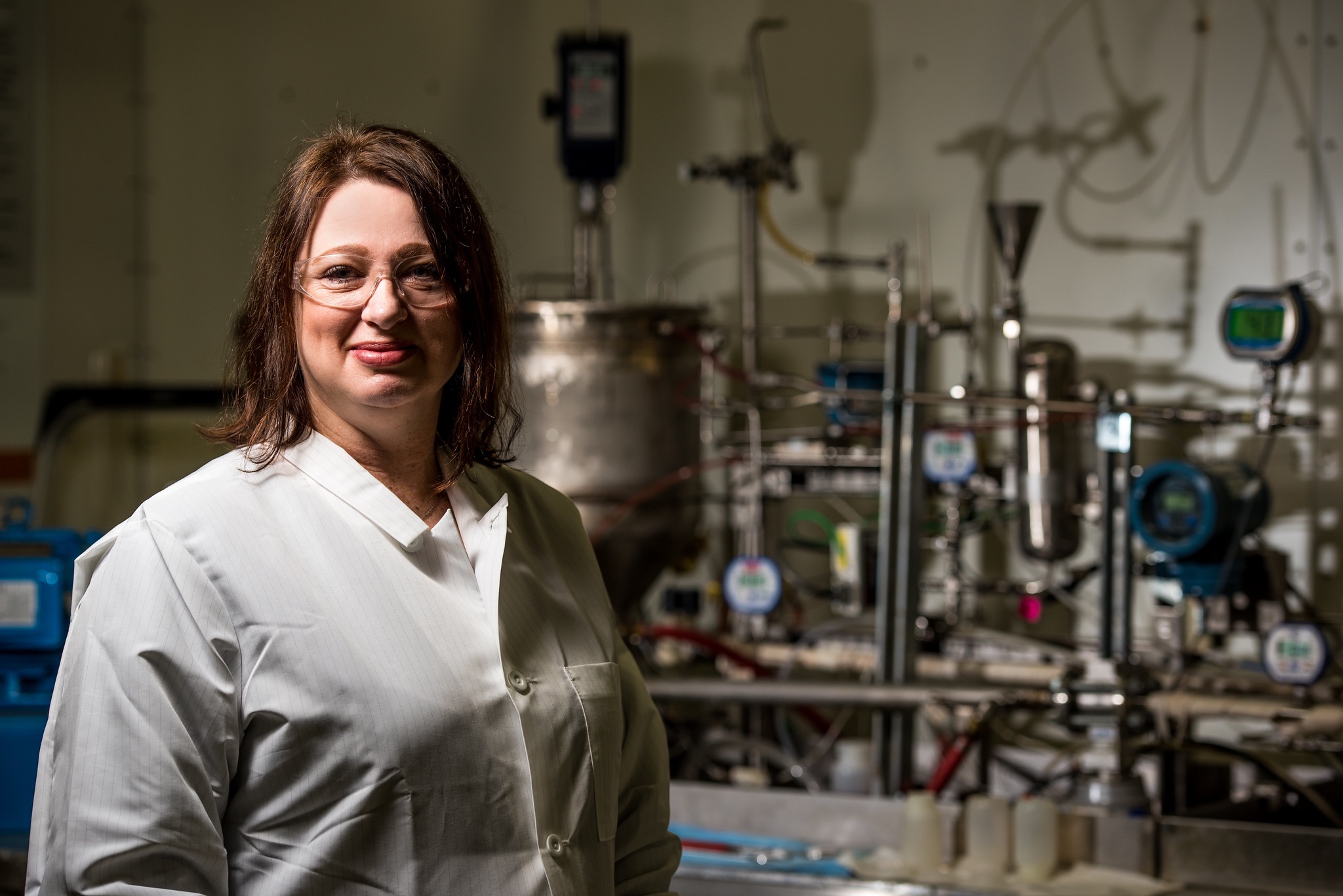 Researcher Carolyn Burns stands next to a laboratory set up of pipes used to test the mesofluidic separator