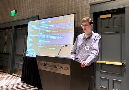 Michael Kieburtz stands at a podium with a projection screen behind him at a conference.