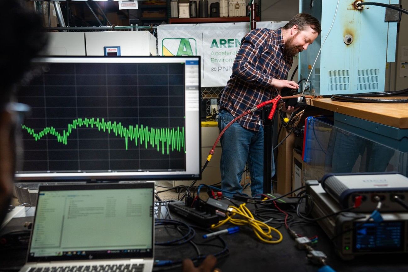 Computer screen with data displayed as man in background uses clam shell coupler on cable