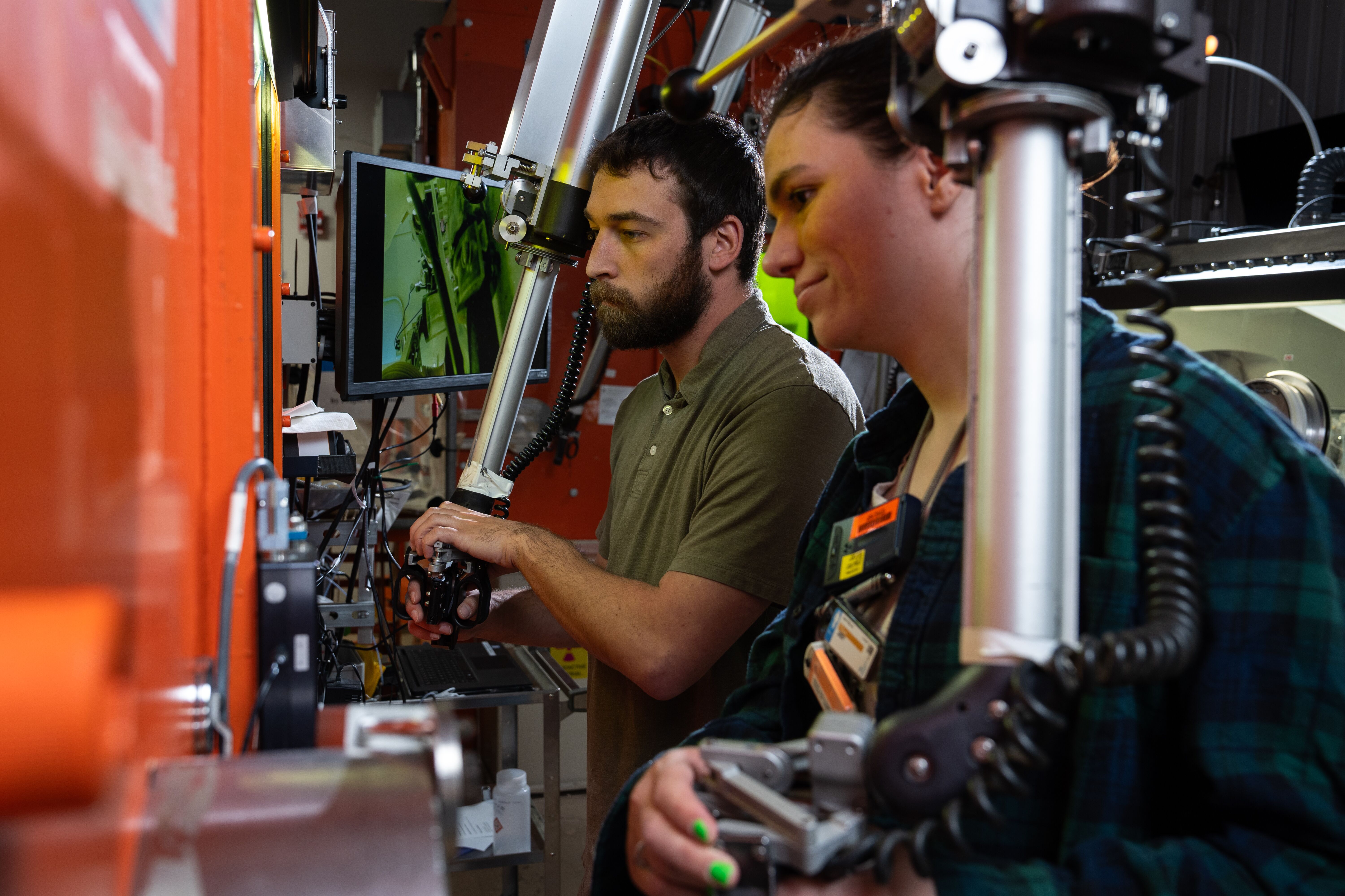 Two nuclear operations technicians inside a facility operating machinery.