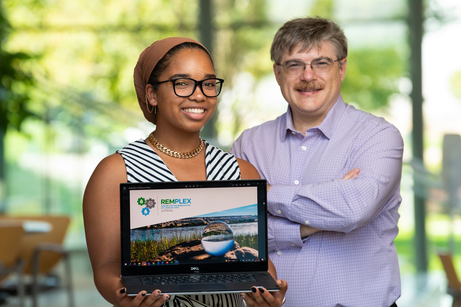 High school intern Jordan Perkins (a young Black woman) holds a laptop showing the RemPlex website, standing next to mentor researcher Chris Johnson (middle-aged white man).