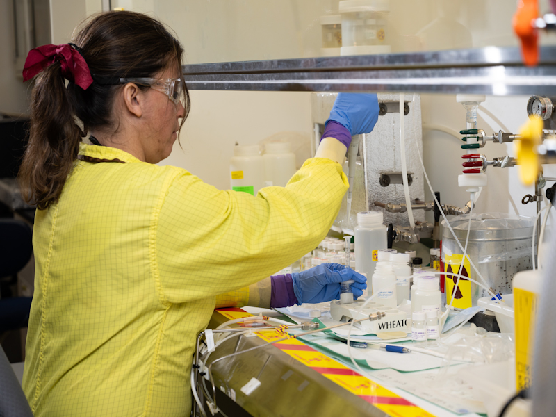 Photo of PNNL Chemist Roberta Rodrigues, wearing safety clothing, goggles, and gloves, using a pipette inside the Radiochemical Processing Laboratory
