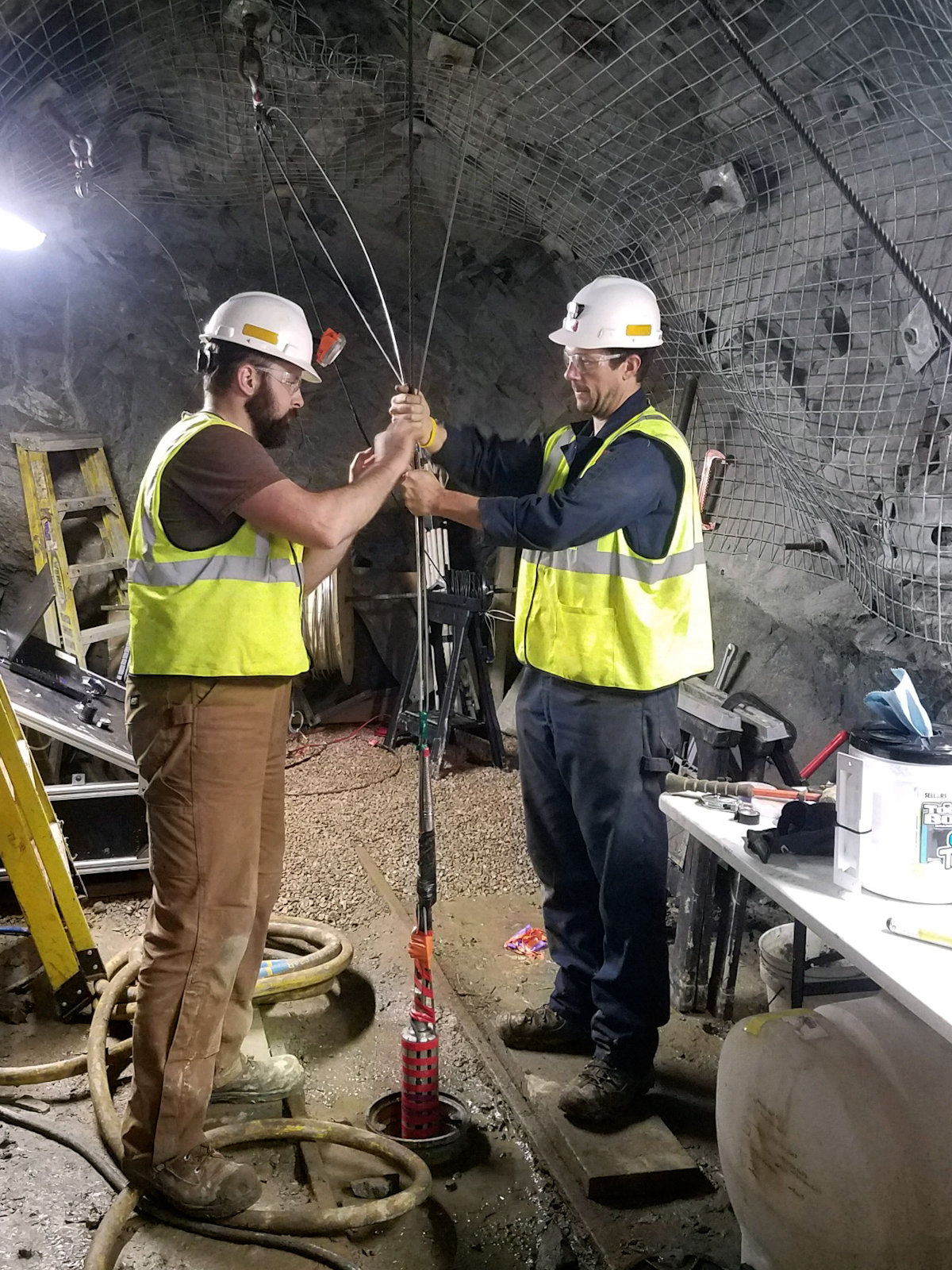 PNNL researcher Jeff Burghardt (left) works at the Sanford Underground Research Facility site with Joseph Pope (right) from Sandia National Laboratories during the EGS Collab experiment. Burghardt and Pope lower a tool into a well on the 4100 level of SURF to make measurements of the stress in the rock.