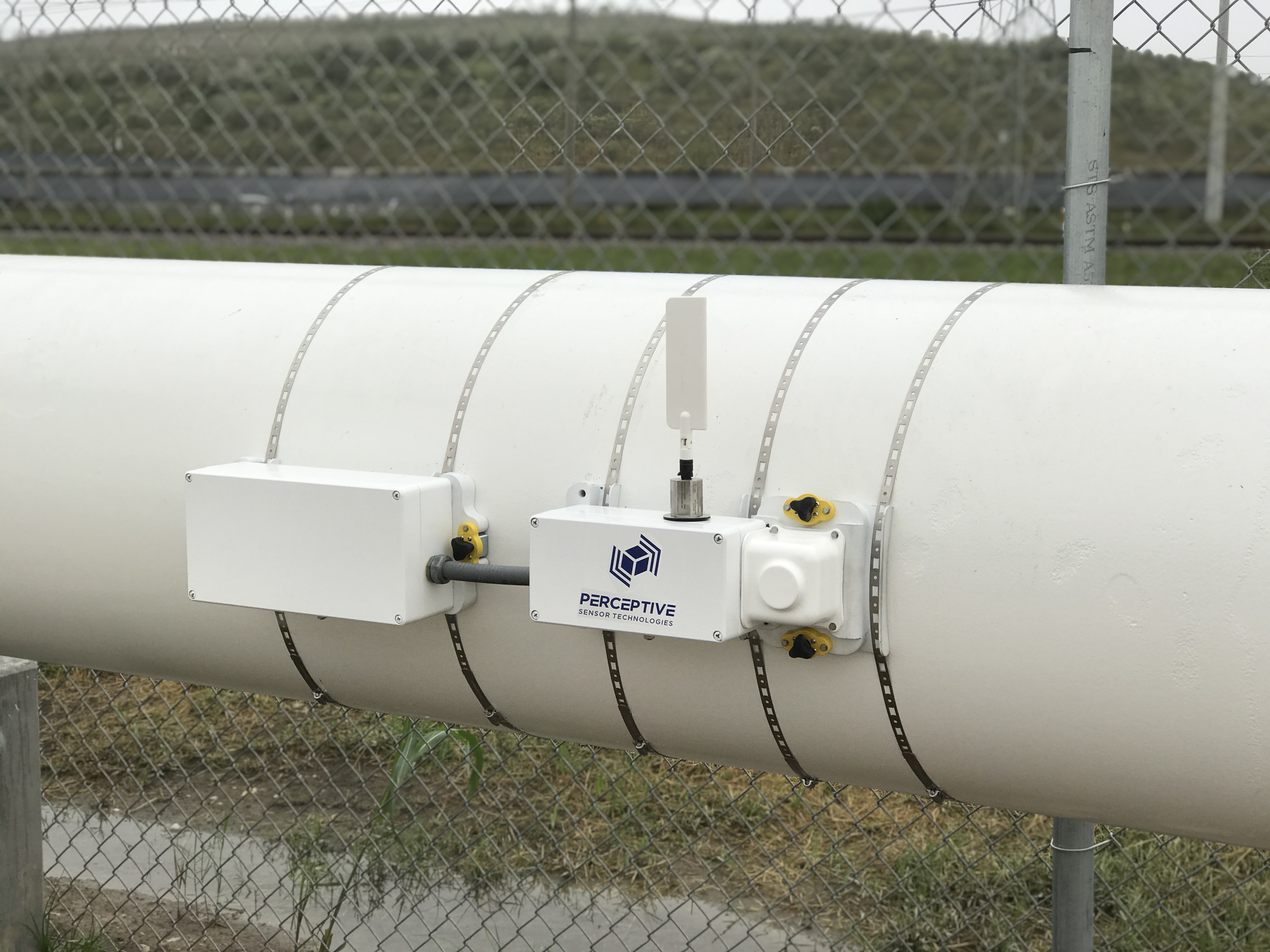 FluID, a fluid-identifying device, sits strapped to the outside of a large pipe. 