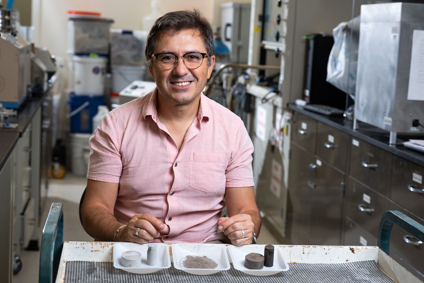 Carlos Fernandez sits behind three samples: a cylinder of conventional cement, a tray of powdered algal biochar, and a cylinder of cement made with algal biochar.