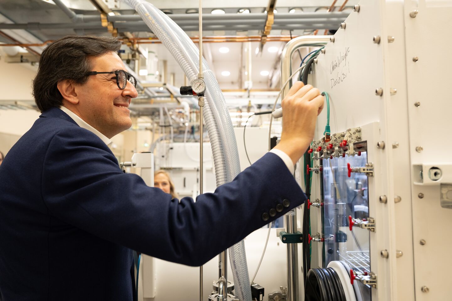Photograph shows a man signing his name on a piece of laboratory equipment.