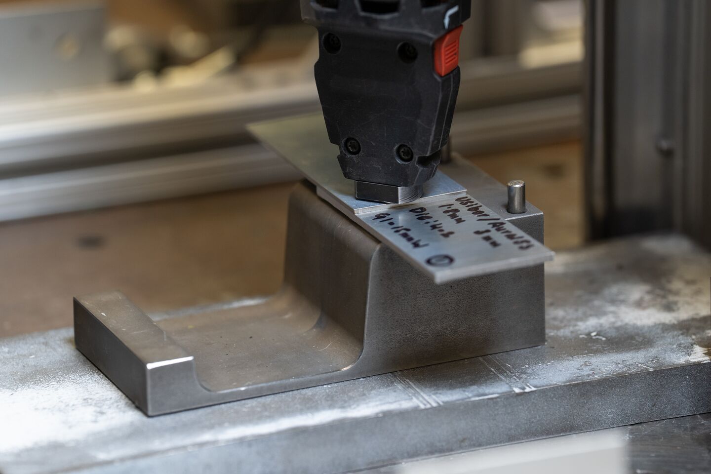 A tip of a joining instrument aligned with a piece of metal and a backing die.