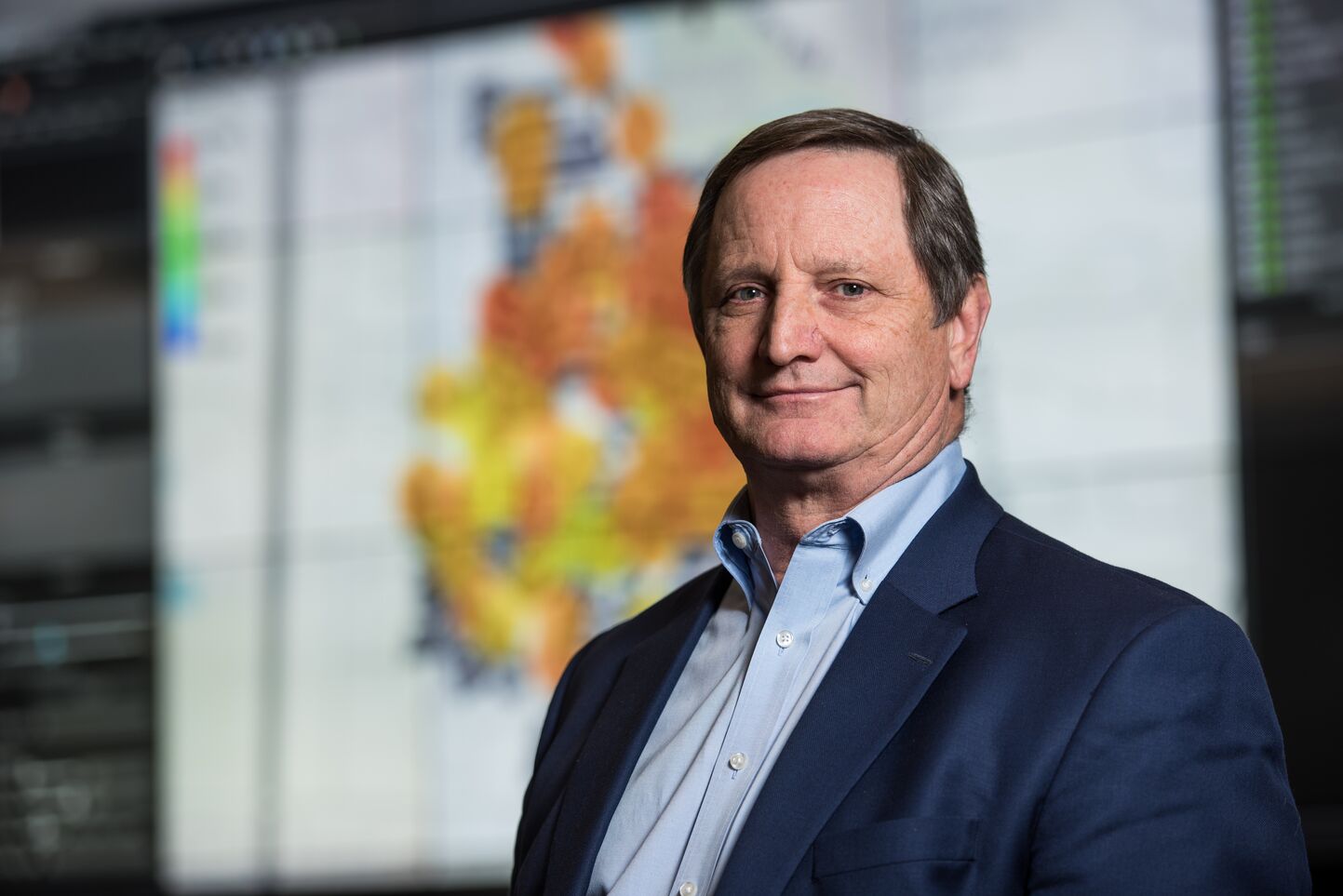 man wearing a blue dress shirt and blue sports jacket is standing in front of map