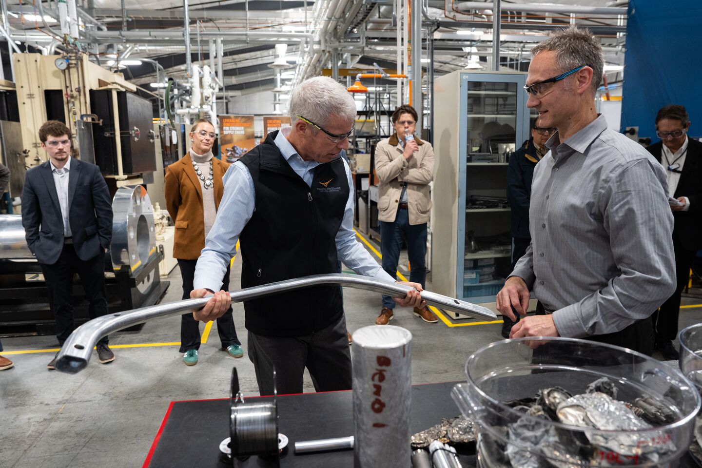 Secretary of Energy Chris Wright holds a large metal object as researcher in safety goggles watch