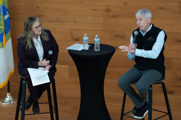 Deb Gracio and Secretary of Energy Chris Wright are seated on stools on a stage with a tall cocktail table between them.