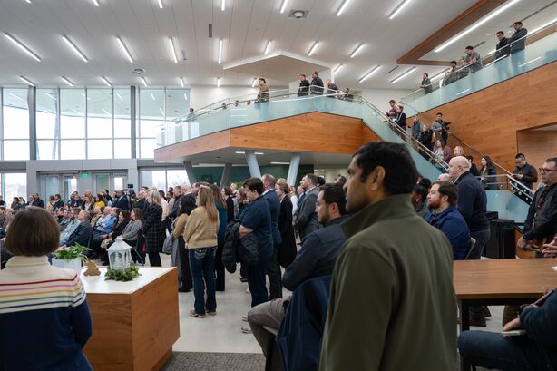 A gathering of PNNL researchers site and stand in a spacious, light-filled lobby watching the fireside chat with Secretary of Energy Chris Wright