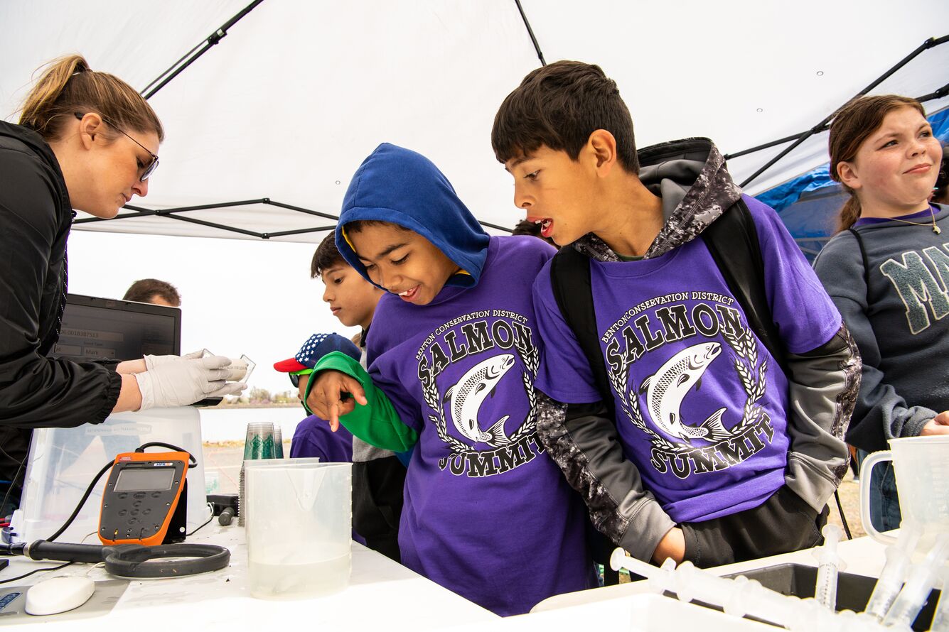 Photo of two students wearing matching purple shirts looking into a container of water