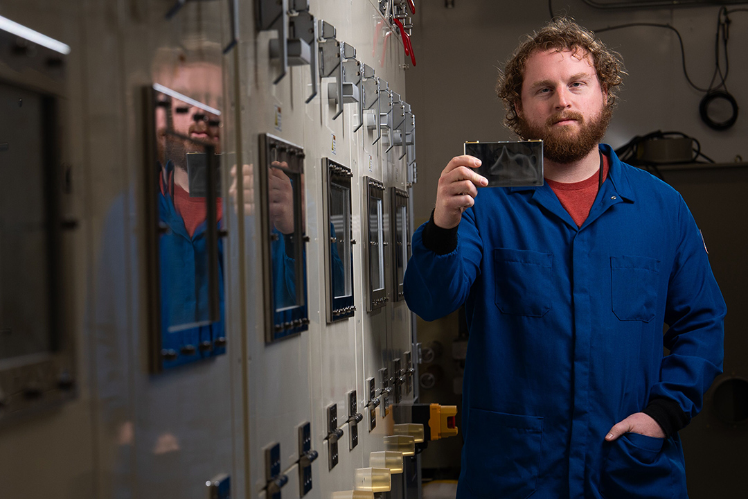 a researcher in a blue jumpsuit holds a battery cell 