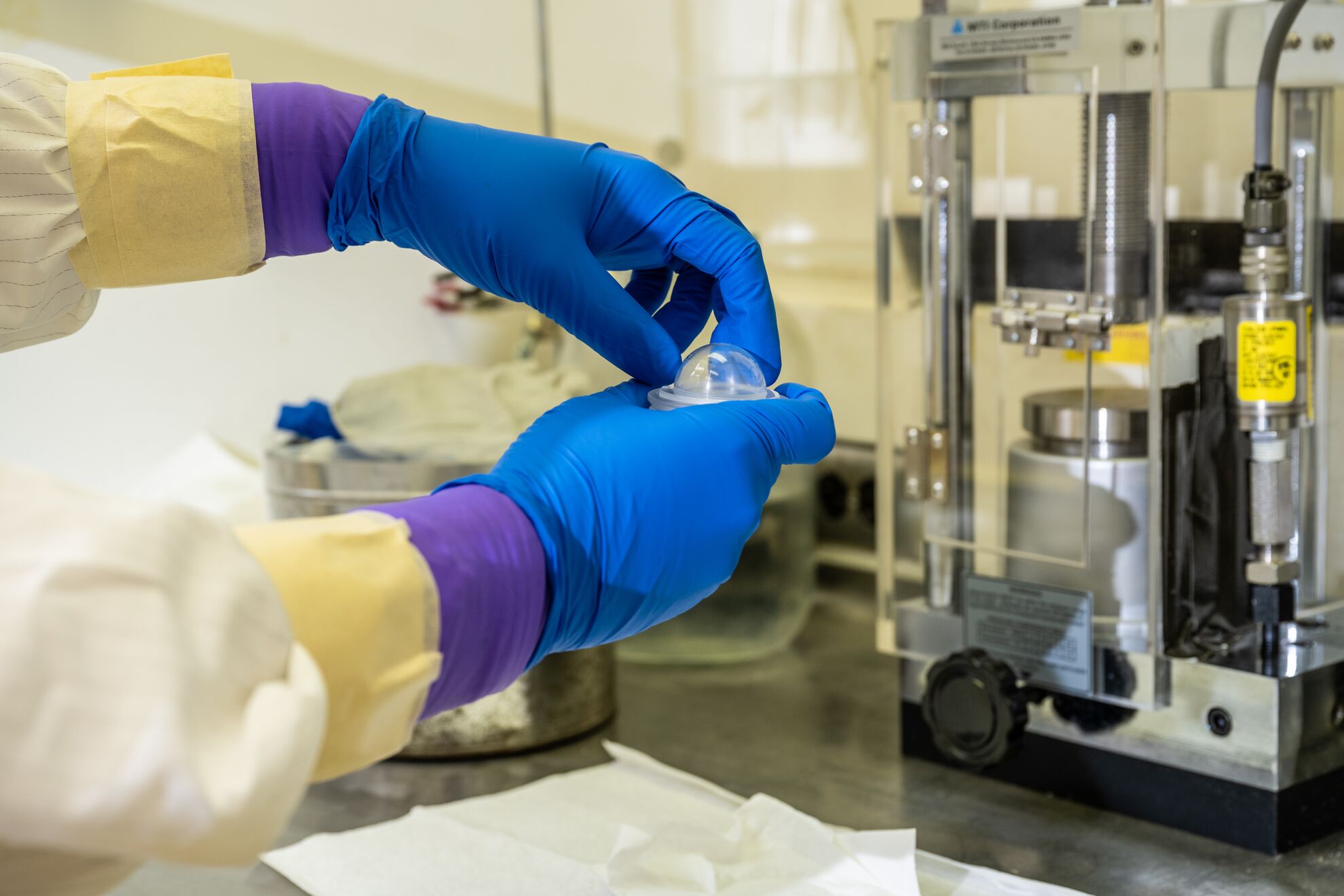 close-focus on a scientist's gloved hands manipulating a small plastic capsule in a lab environment