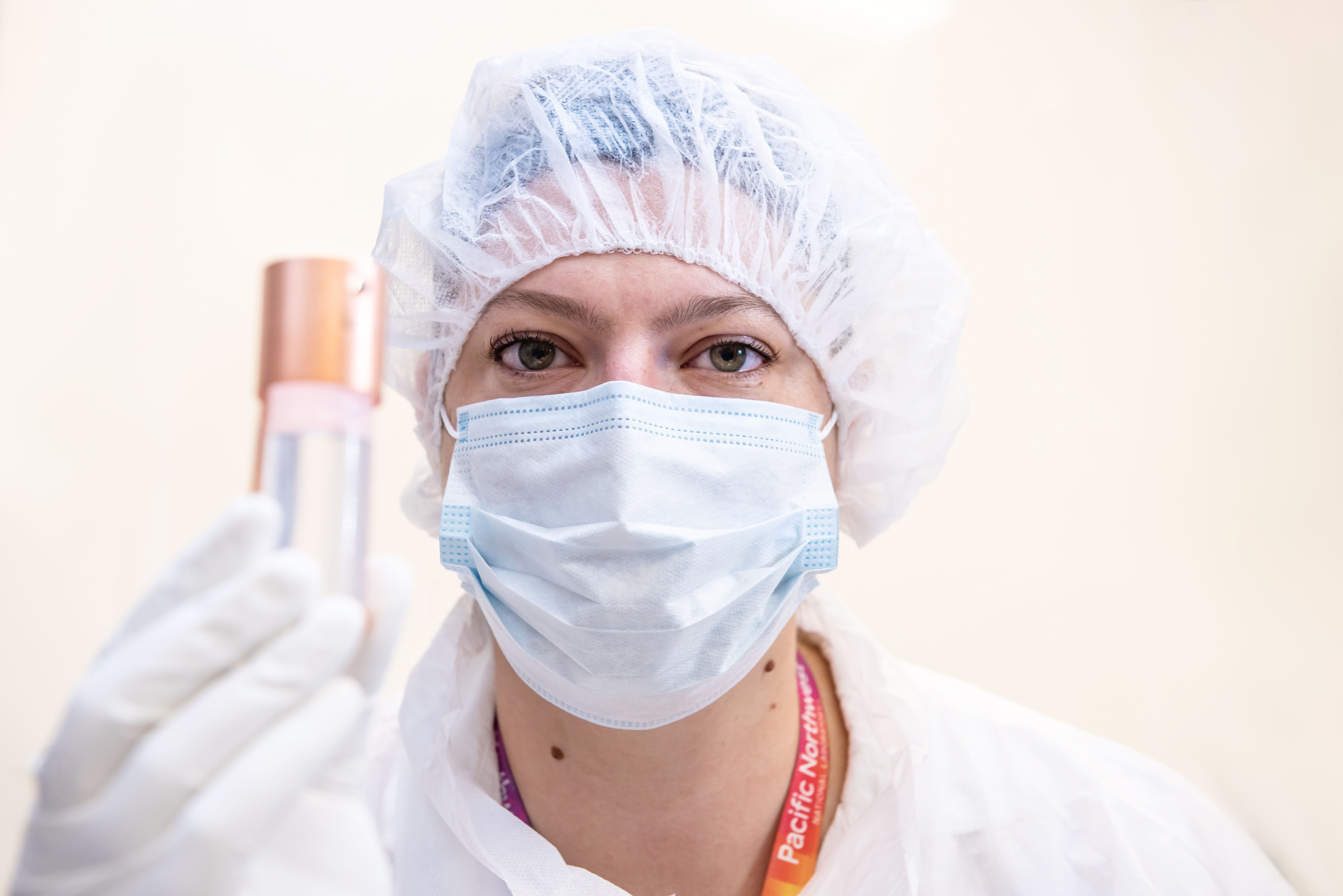 Photo of PNNL physicist Stephanie Lyons holding up a small clear tube with a copper top, known as a ultra-low background Liquid Scintillation Detector.