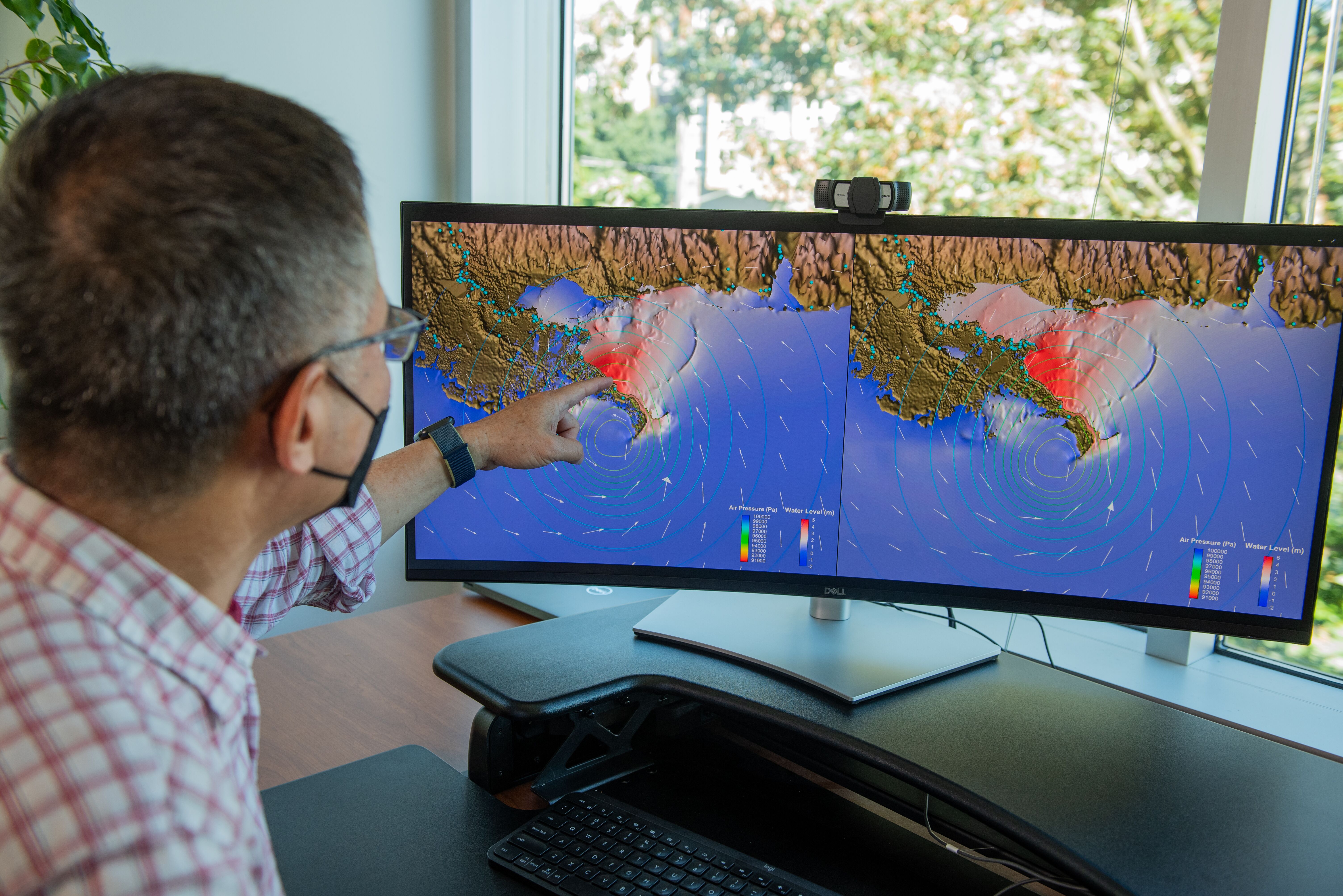 Photo of a researcher pointing to a coastal model on a computer monitor.