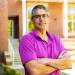 Photo of a man in a magenta shirt with arms crossed. 