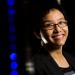 Smiling Asian woman with short hair and glasses and a dark background with blue lights