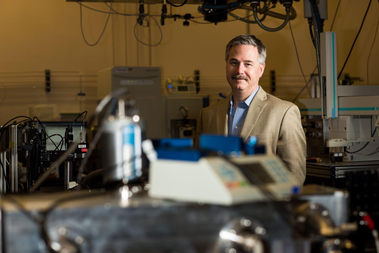 man in beige suit jacket behind lab equipment