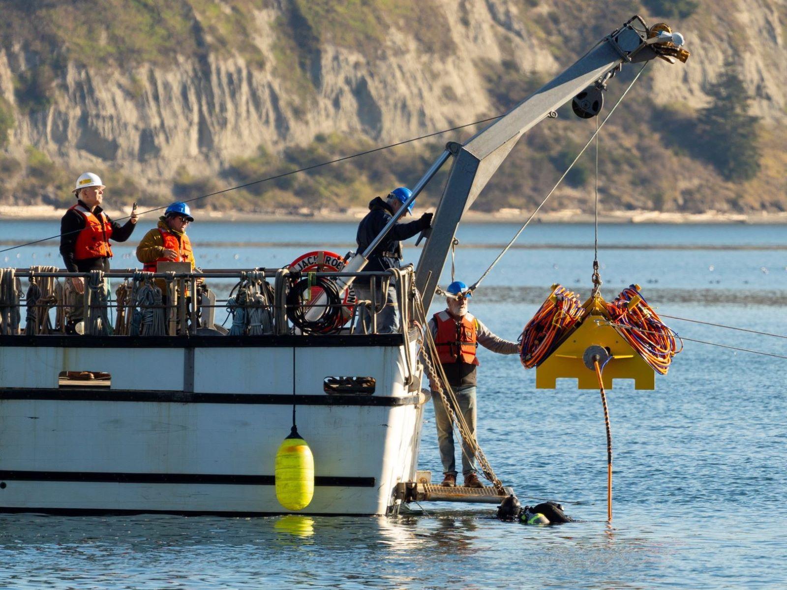 a research boat with a crane lowering the CRABEE node of wiring to the surface of Sequim Bay