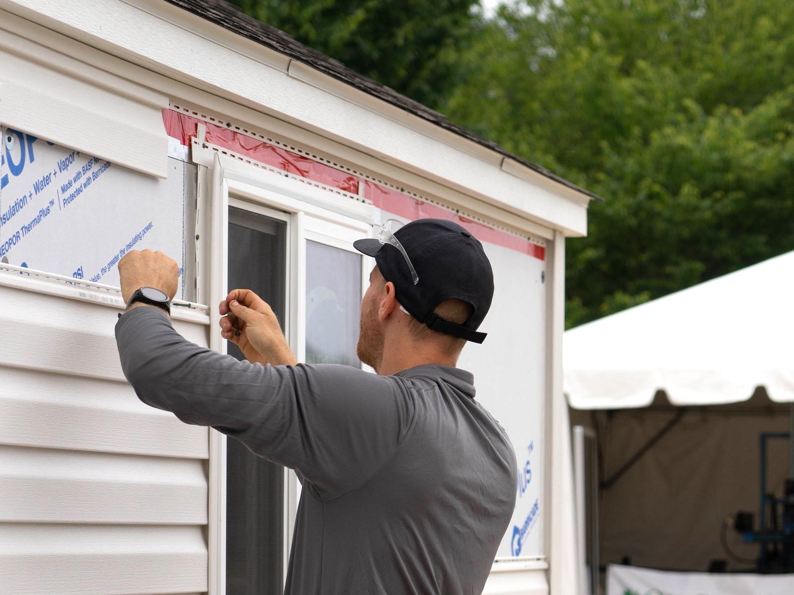 Person installing new siding over new insulation on an exterior wall.