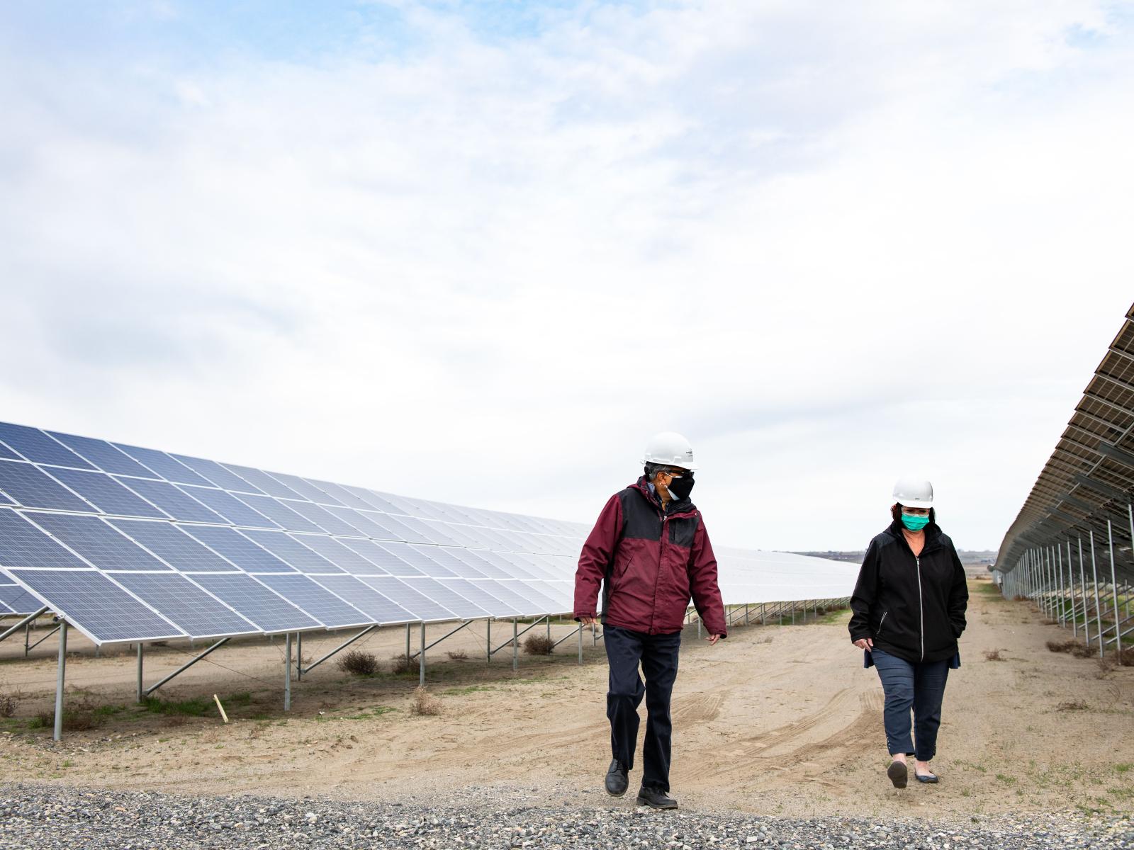 Two people walk beside a row of solar panels in Washington.