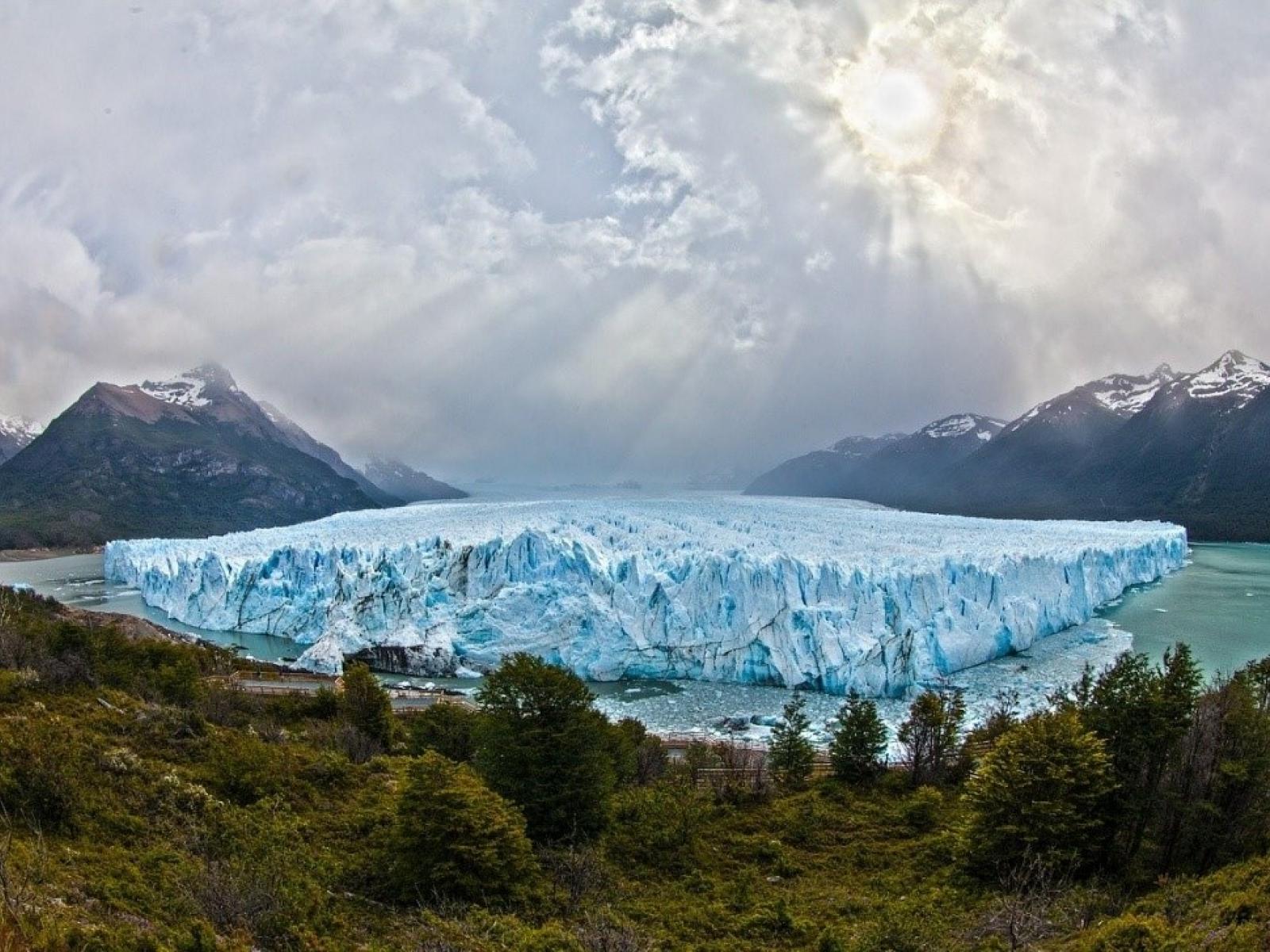 A glacier centered in a lake, surrounded by mountains and trees.