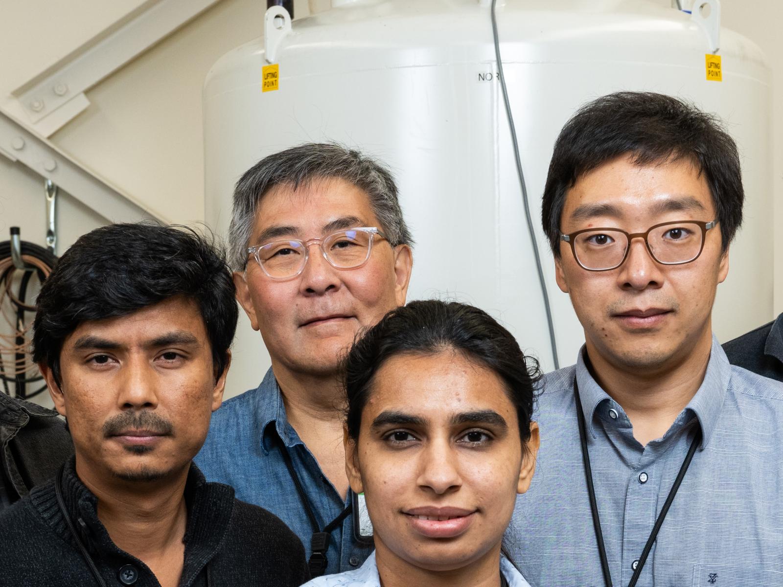 Photograph close up of the faces of four researchers standing in front of an NMR