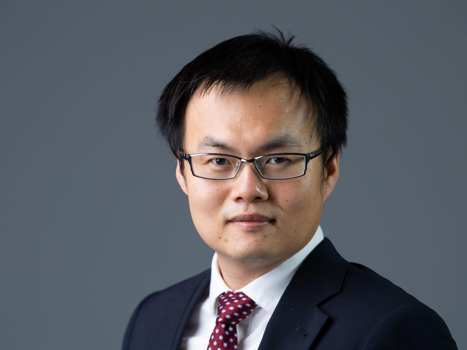 Man wearing glasses with dark sports jacket, white shirt, and multi-colored tie.