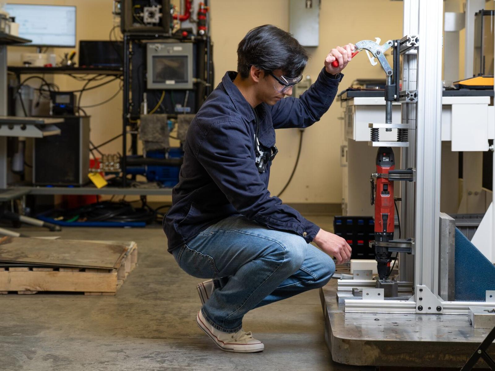 A man kneels in front of a manufacturing instrument, setting it up for operations.