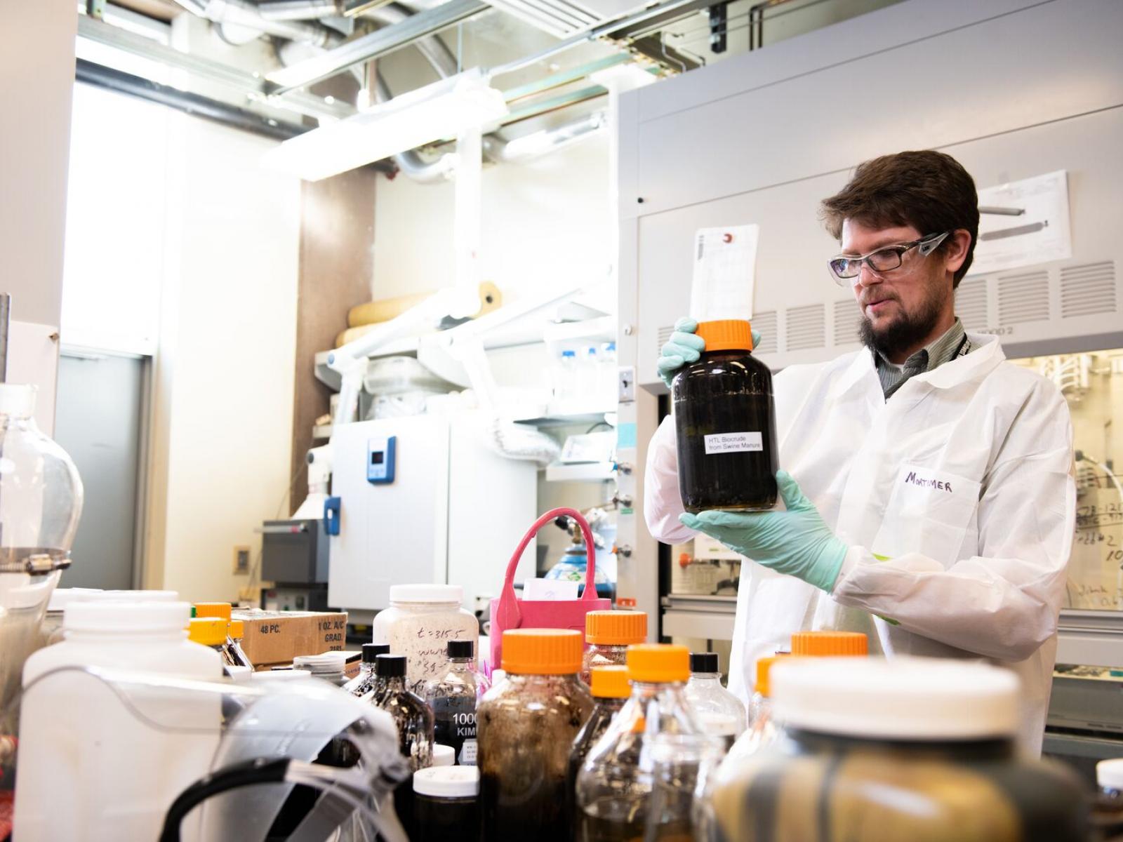 Man in lab coat holding jar of swine poop.