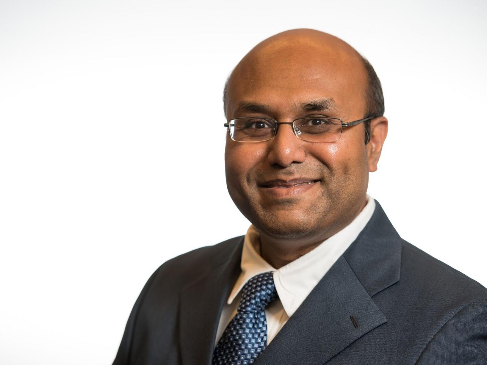 Image of slightly smiling Asian man with glasses in a suit and tie