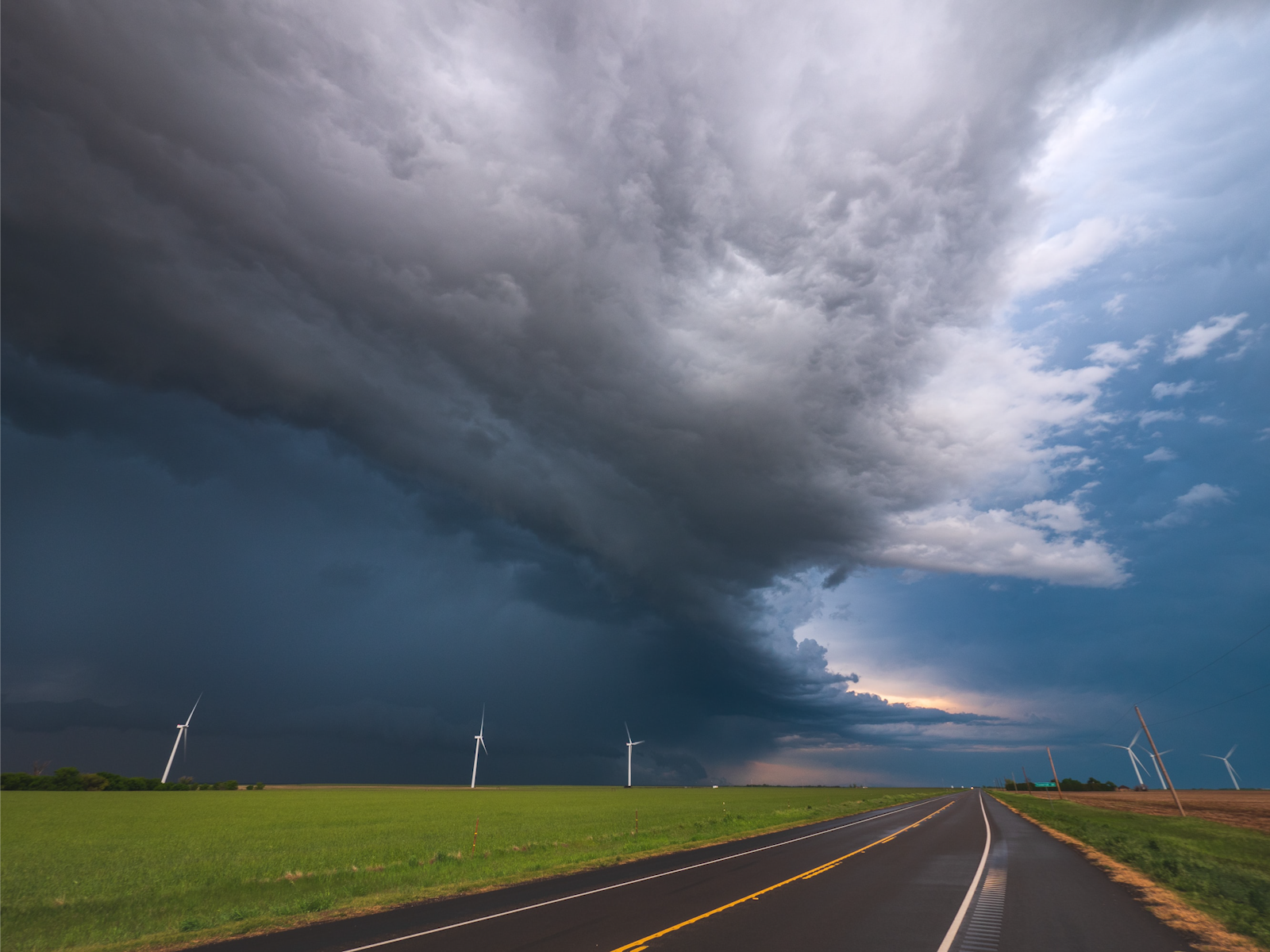 Photograph of a storm cloud over a road and windmills.