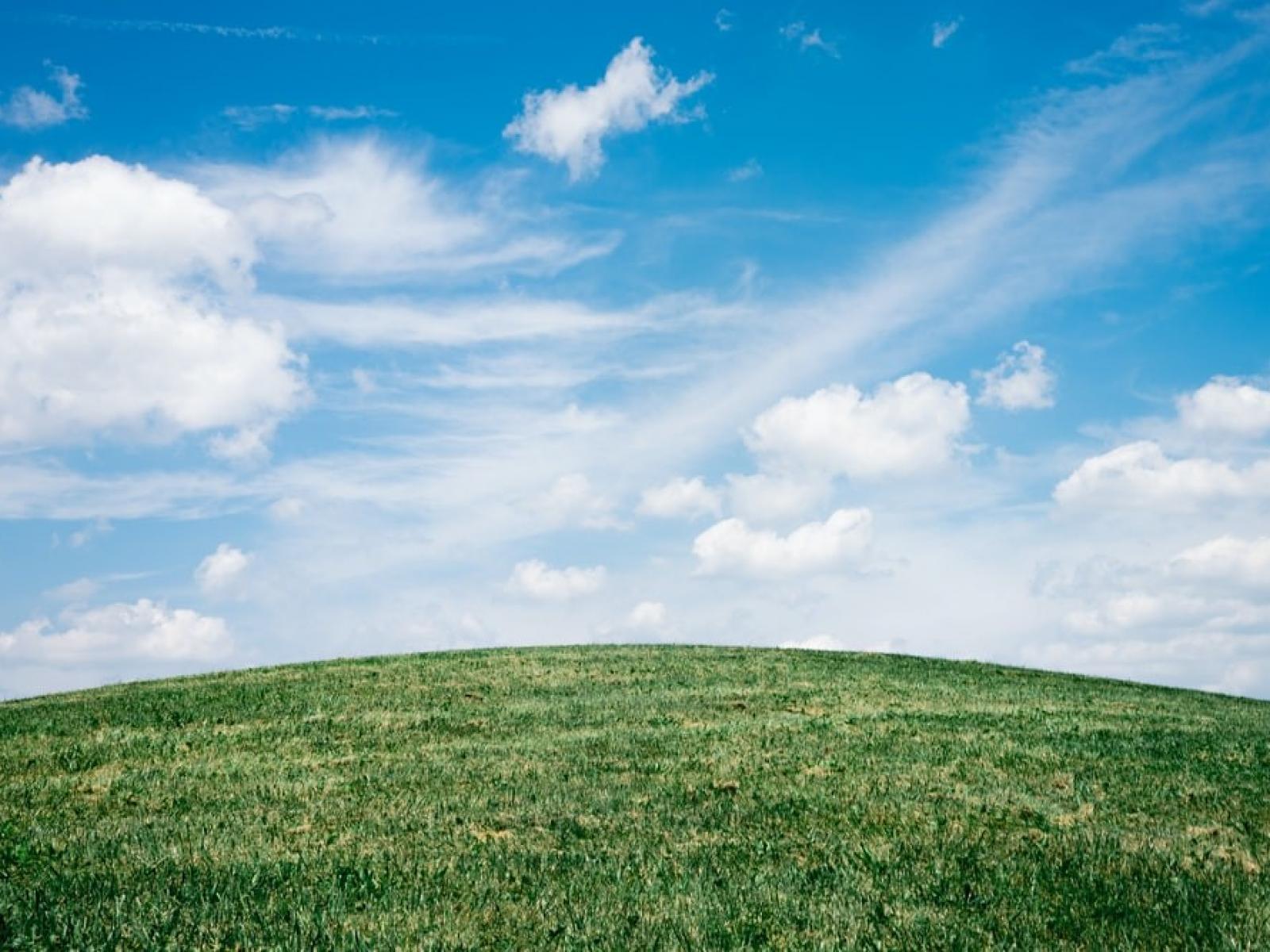 Clouds on a bright blue sky above a grassy hill