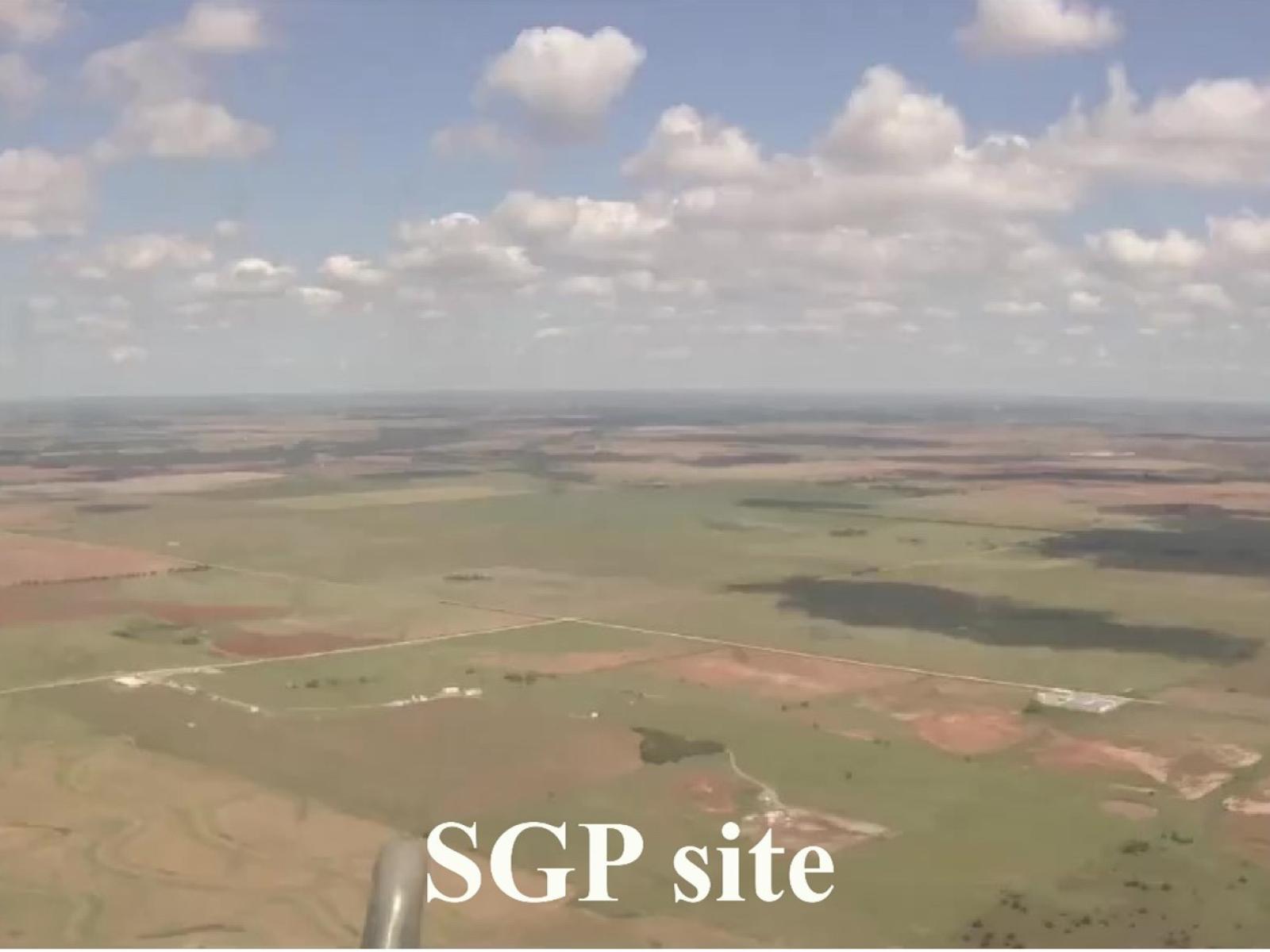 Photograph out the window of an airplane showing green and brown fields along with clouds