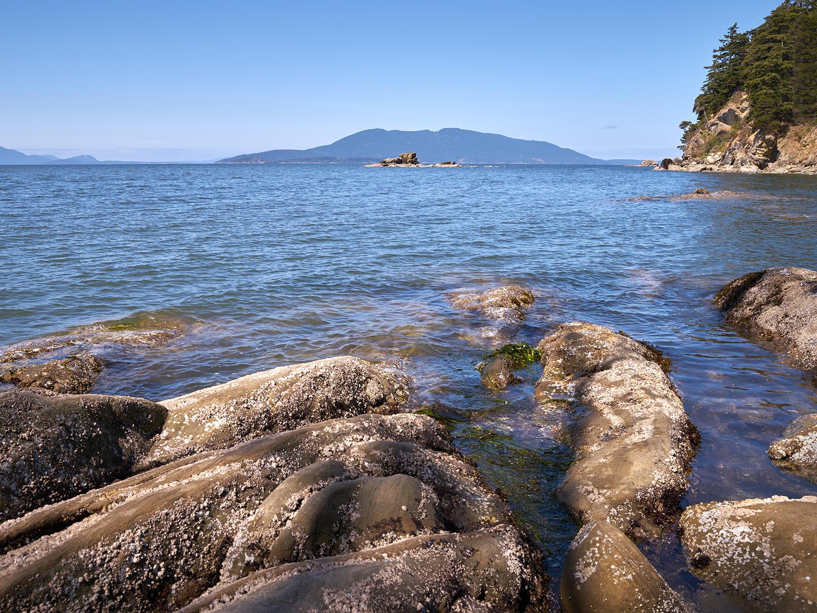 Rocky shoreline looking out to water with mountain range in background.
