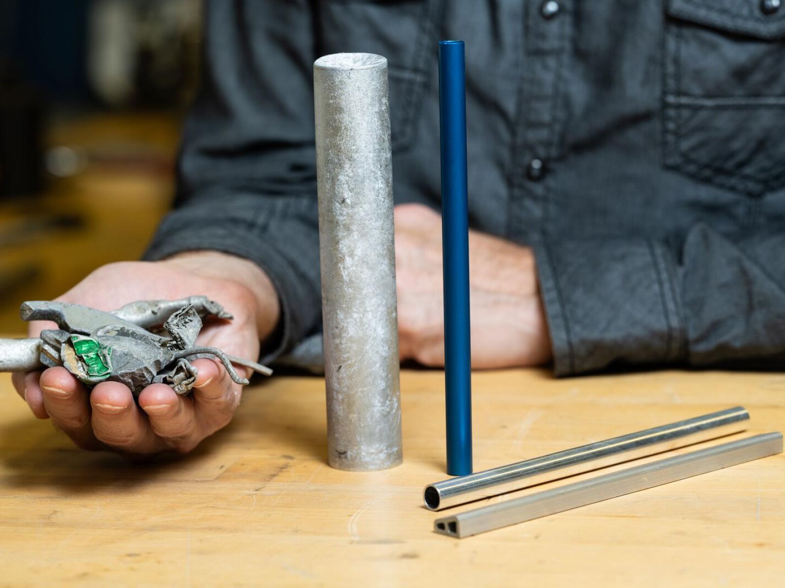 Photo of a person holding a pile of aluminum scrap next to four cylinders of recycled aluminum scrap